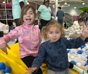 Girls in ball pit waving and smiling at camera